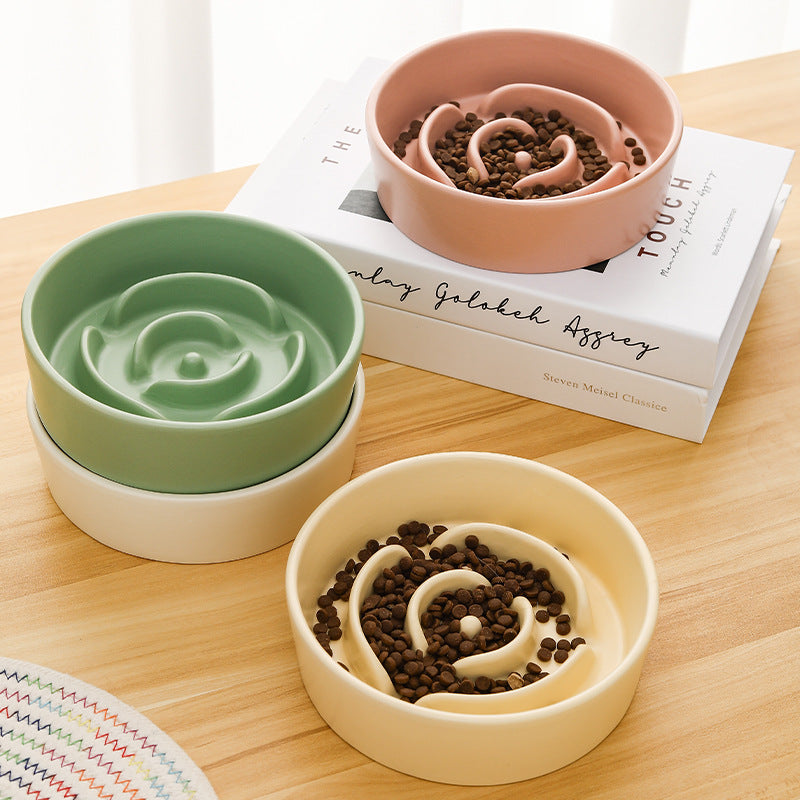Three pet bowls in green, pink, and beige on a wooden surface with books underneath.