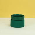 Green ceramic bowl on a white surface with a yellow background