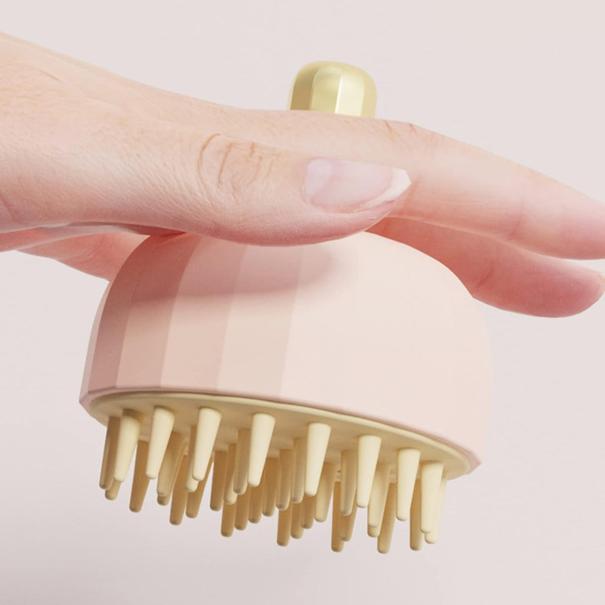 Hand holding a pink scalp massager with gold bristles on a light background
