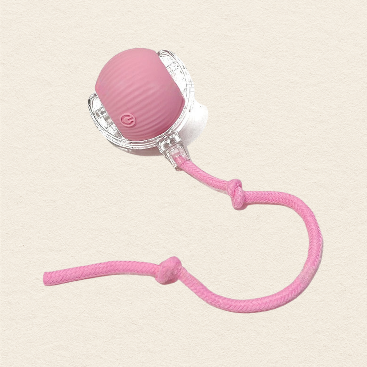 A pink textured silicone cat toy with a clear plastic frame and a pink braided cord, shown on a textured beige background.