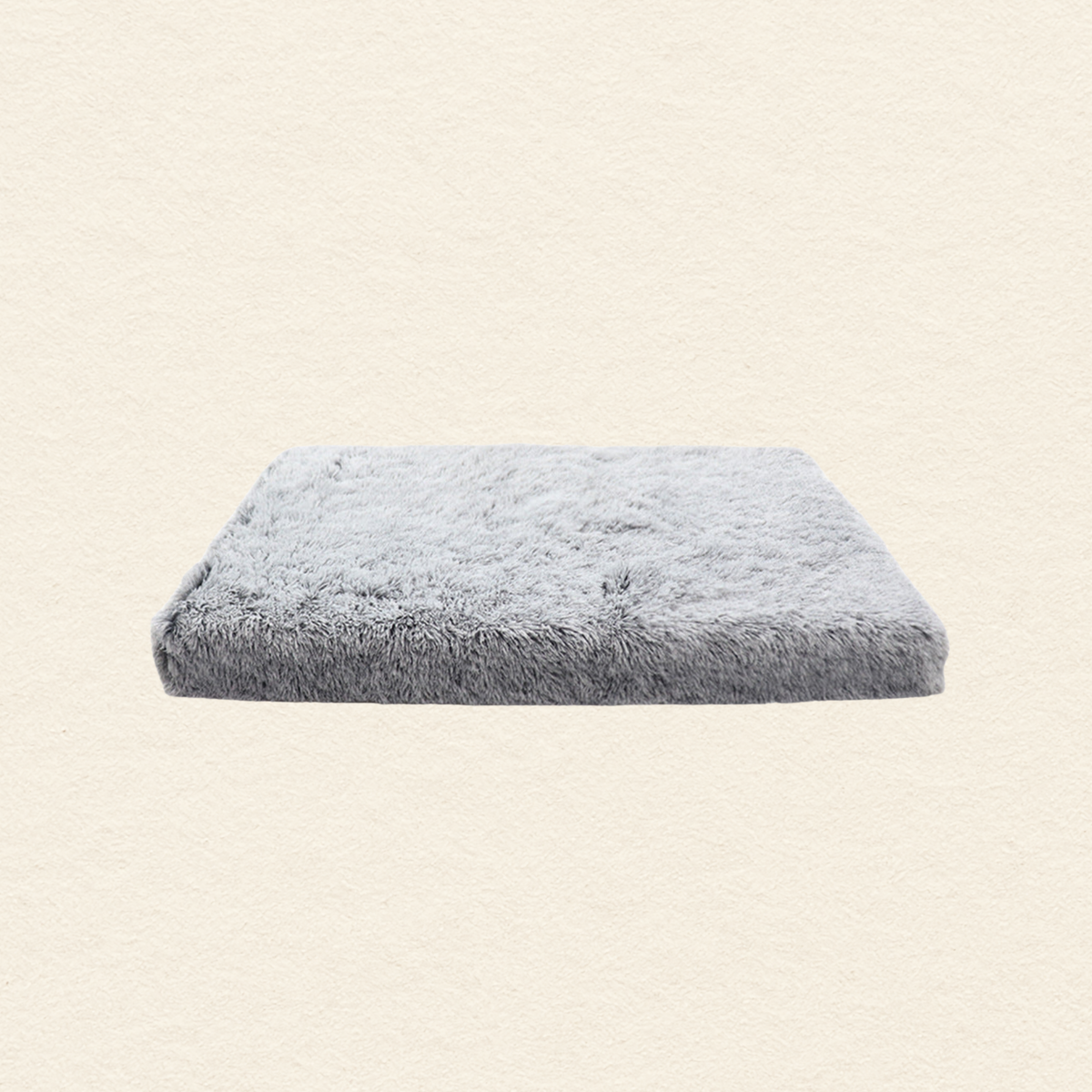 A rectangular, fluffy light gray pet bed or cushion with a soft, shaggy texture, shown against a plain, textured off-white background.