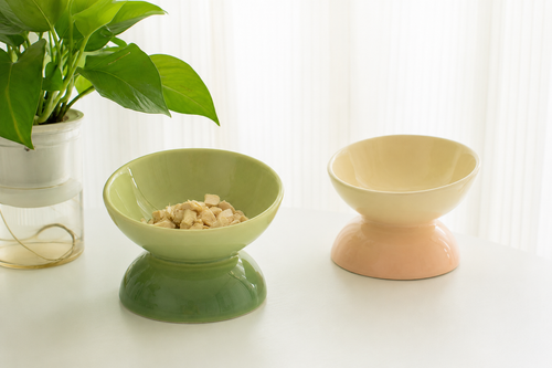 Two ceramic pedestal bowls. One bowl is light green with a darker green base, while the other is cream with a peach-pink base.