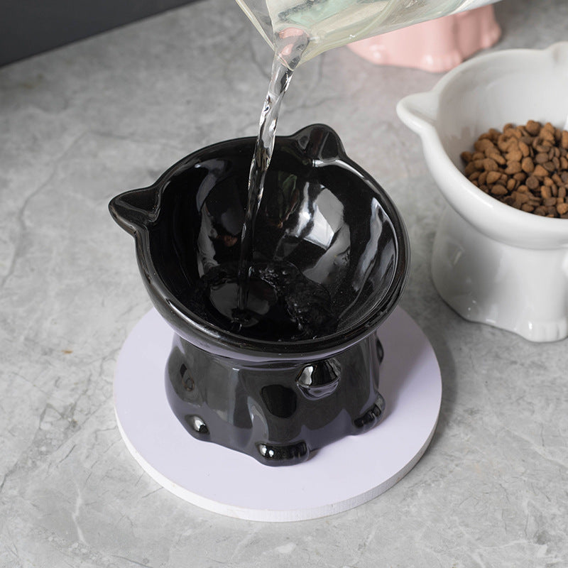 Black ceramic cat-shaped water bowl on a gray surface with a white bowl of food in the background.