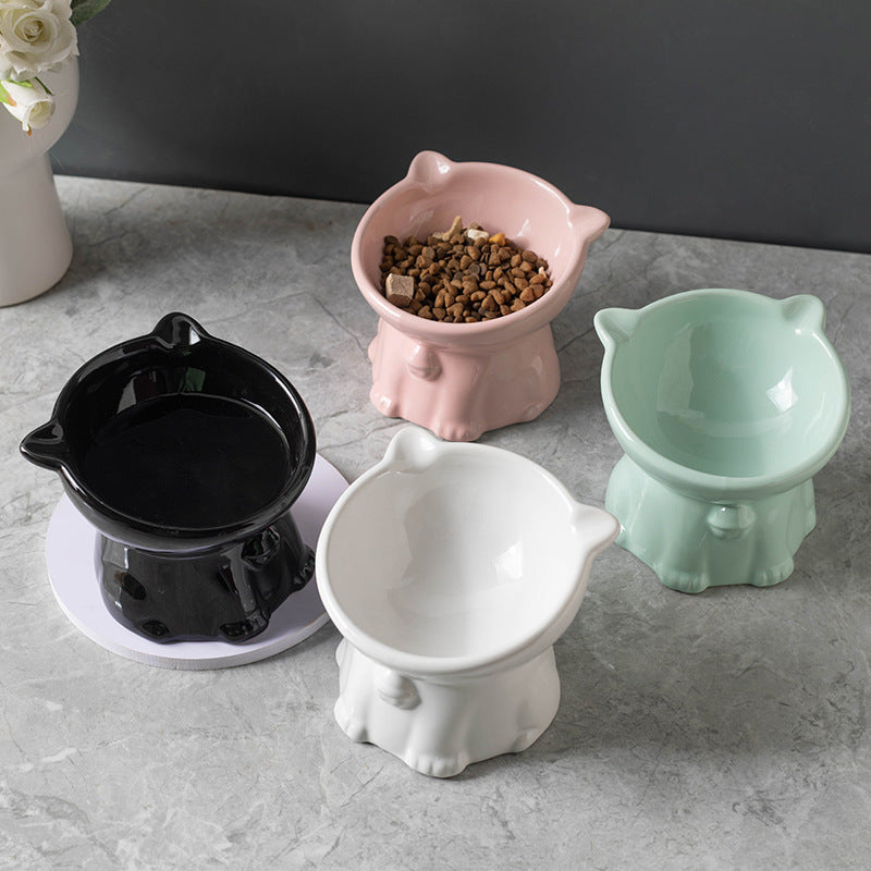 Set of four ceramic pet bowls in black, pink, white, and green on a gray surface.